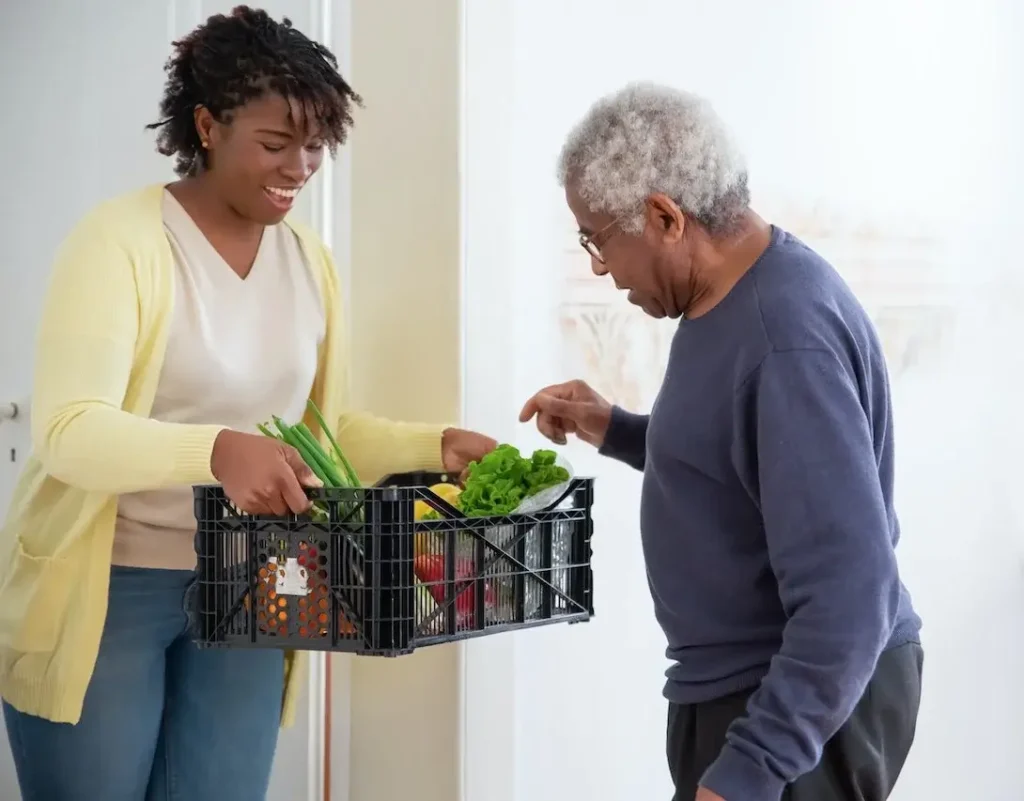 A Woman carer Holding a Plastic Crate with Fruits and Vegetables for old-aged person